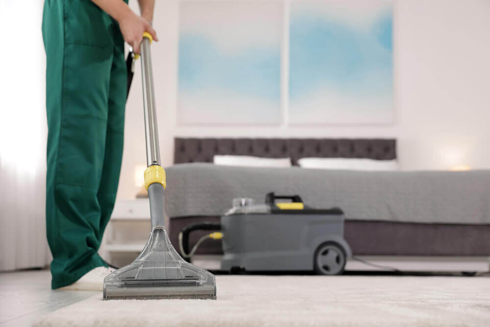 A carpet cleaning Toowoomba worker in green overalls cleaning a white carpet with a wet vaccume