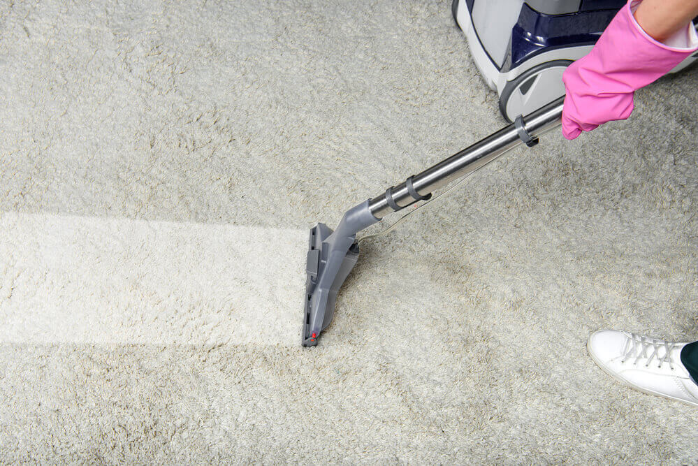 a carpet shampooer worker cleaning a white carpet whilst wearing pink gloves