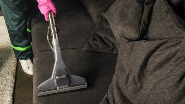 top down shot of an upholstery cleaner cleaning a black couch with bright pink washing gloves on